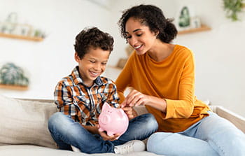 mother and son sitting on a couch looking at a piggy bank