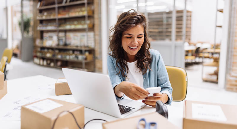 women at computer looking at a phone