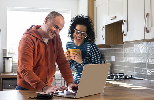 Two people smiling at a laptop in a kitchen