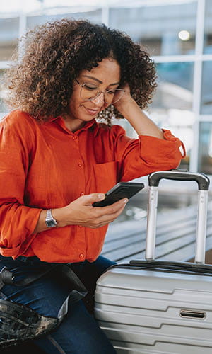 woman looking at her phone next to her suitcase