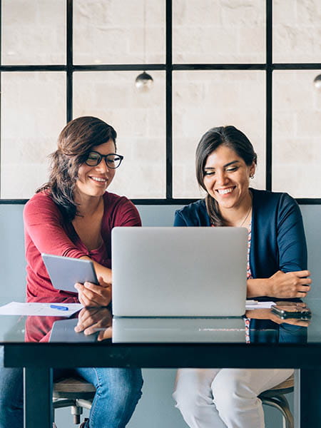 Two colleagues looking at a laptop with a tablet in hand