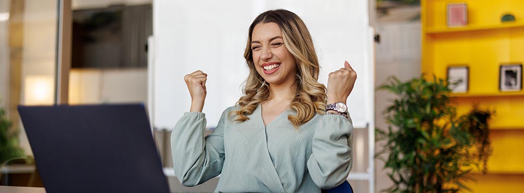 Person smiling at laptop with hands in the air