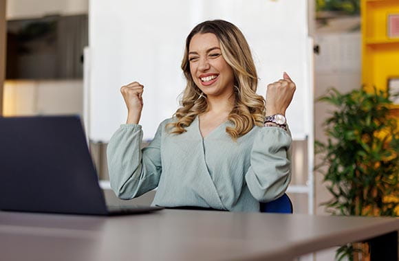 Person smiling at laptop with hands in the air