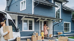Person carrying boxes to a home surrounded by moving boxes