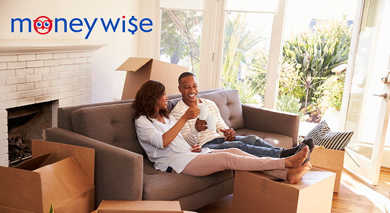 Two people on couch holding mugs surrounded by moving boxes