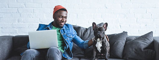 man sitting on a couch with his dog and a laptop