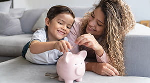 Child putting coins into piggy bank with parent assist