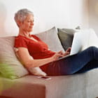 Woman types on laptop while relaxing on couch