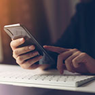 person using their cell phone over their computer keyboard