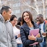 Five college students walking on campus outside smiling and carrying books