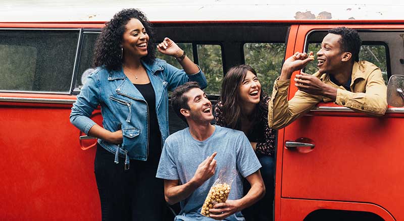 Four friends pause for a roadtrip carmel corn break in a red VW van