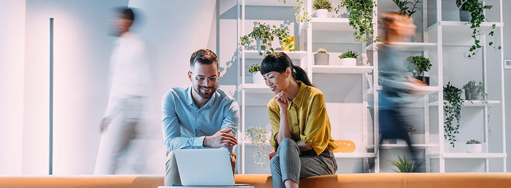 Two colleagues in an office space looking at a laptop