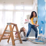Mother paints bedroom blue with a roller brush while daughter looks on