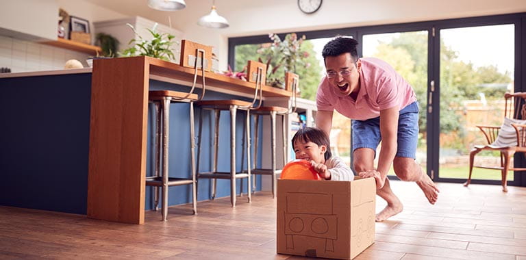Father pushing son in cardboard box at home