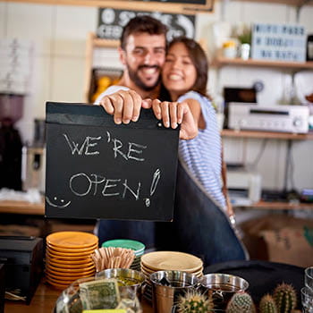 Small cafe owners holding up a sign saying "we're open"